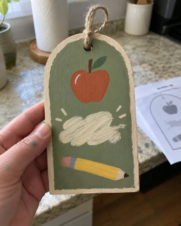 A finished hand-painted teacher name door hanger on a porch table